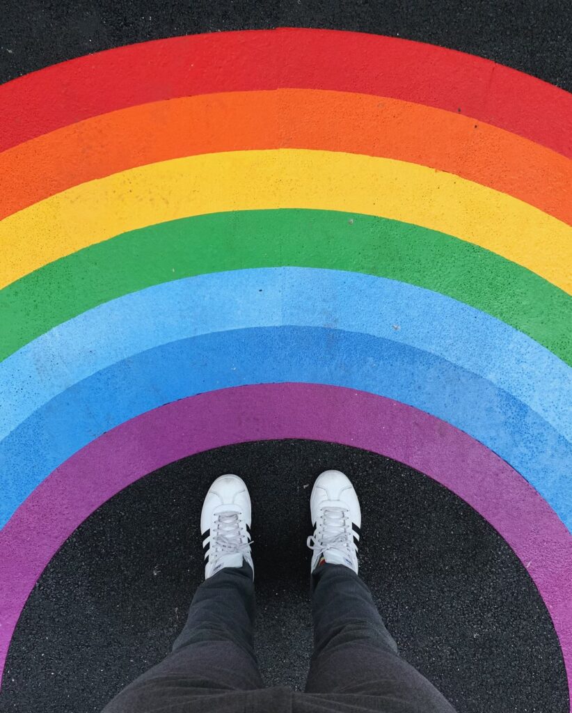 Image of a person standing on a pride painted sidewalk with pride colors. 